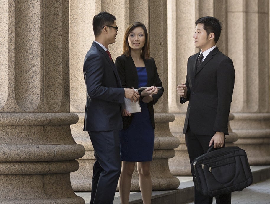 three tax audit representation professional dressed in business clothing, two males and one female, standing in front of columns